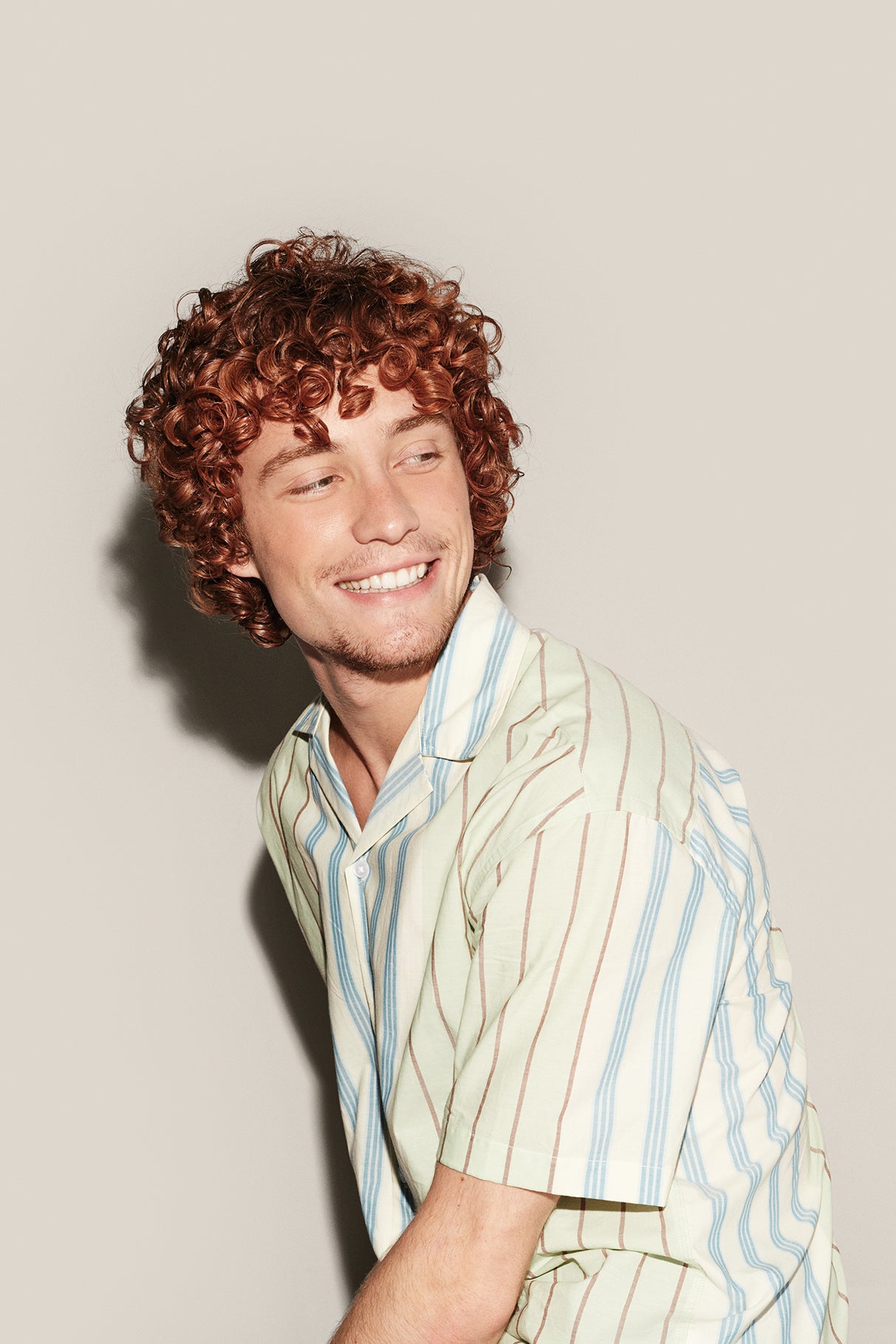 Man with curly hair wearing a striped shirt against a plain background