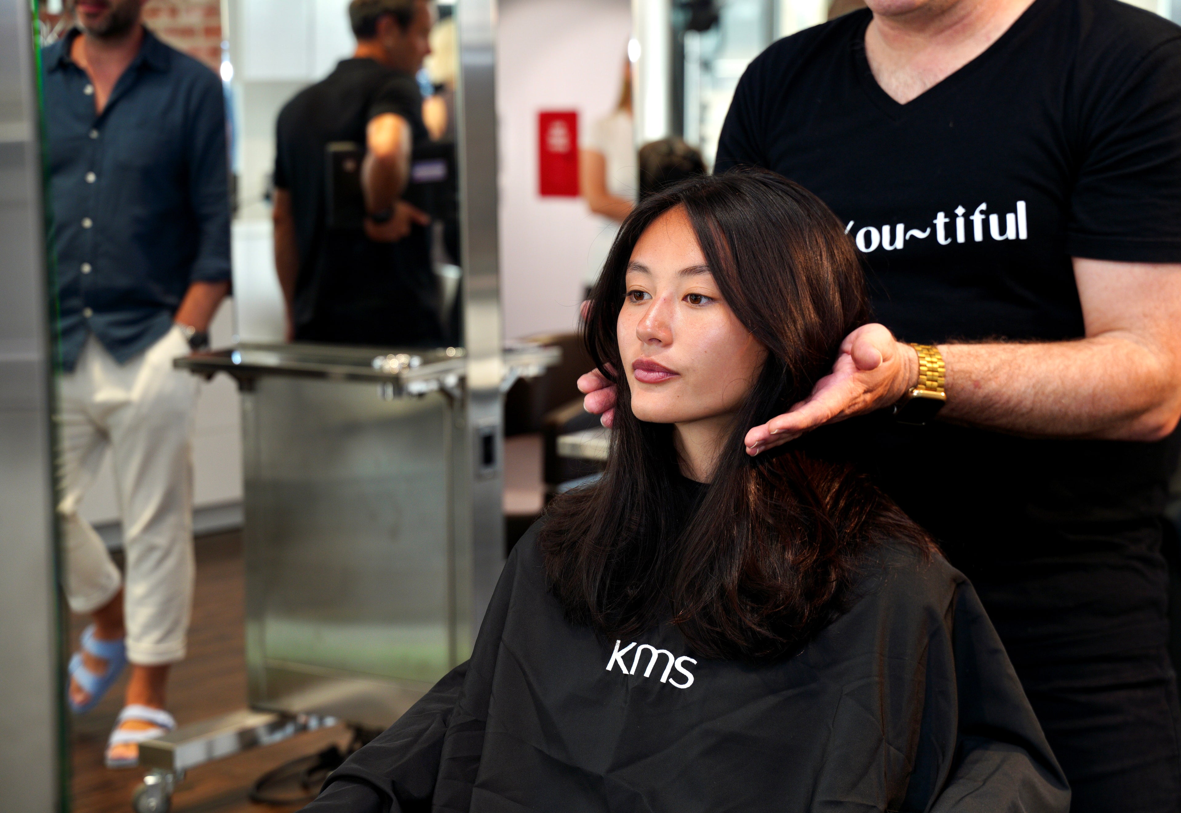 Person getting a haircut in a salon with another person styling their hair.