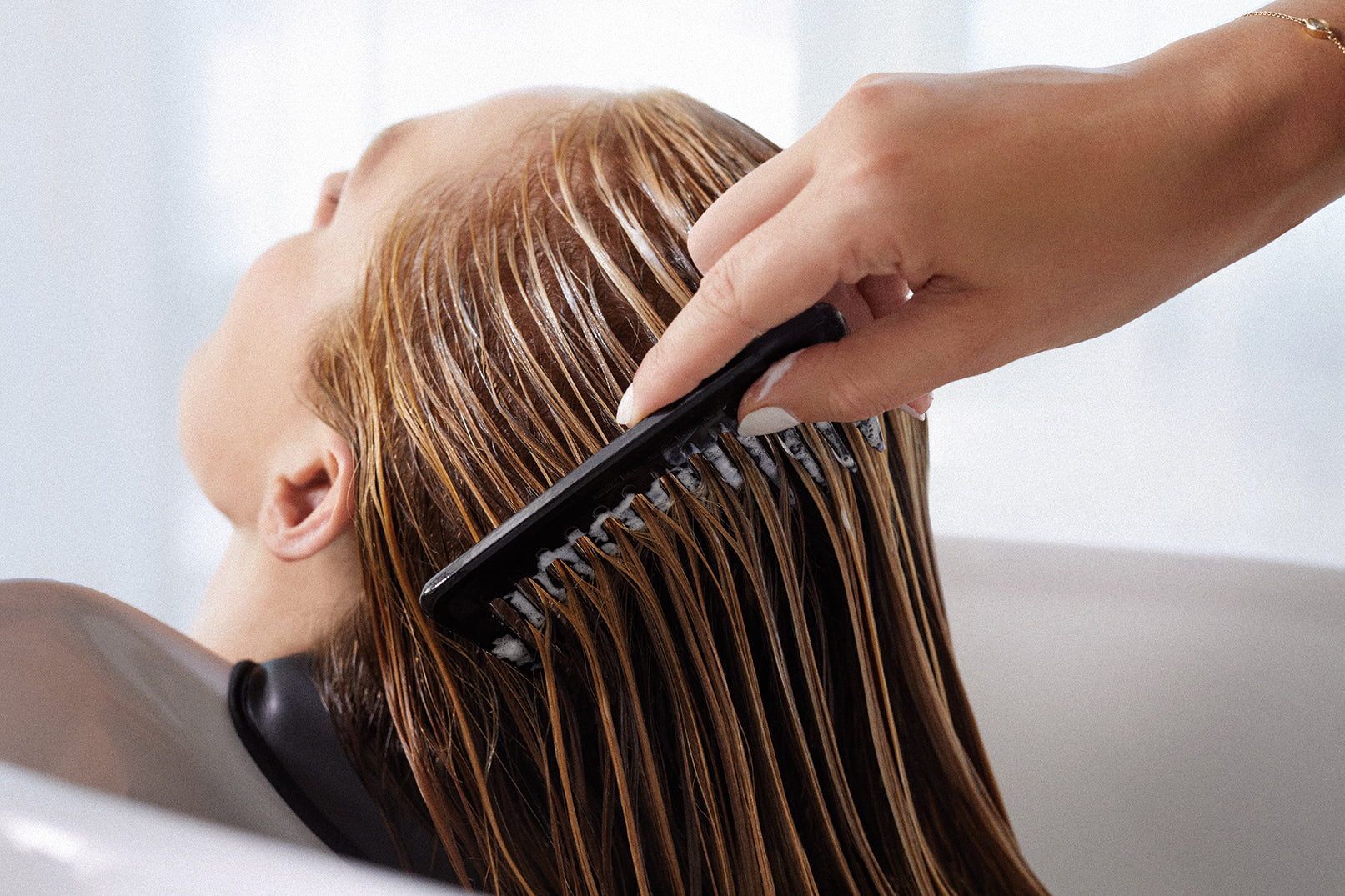 Person washing hair with a comb in a salon setting