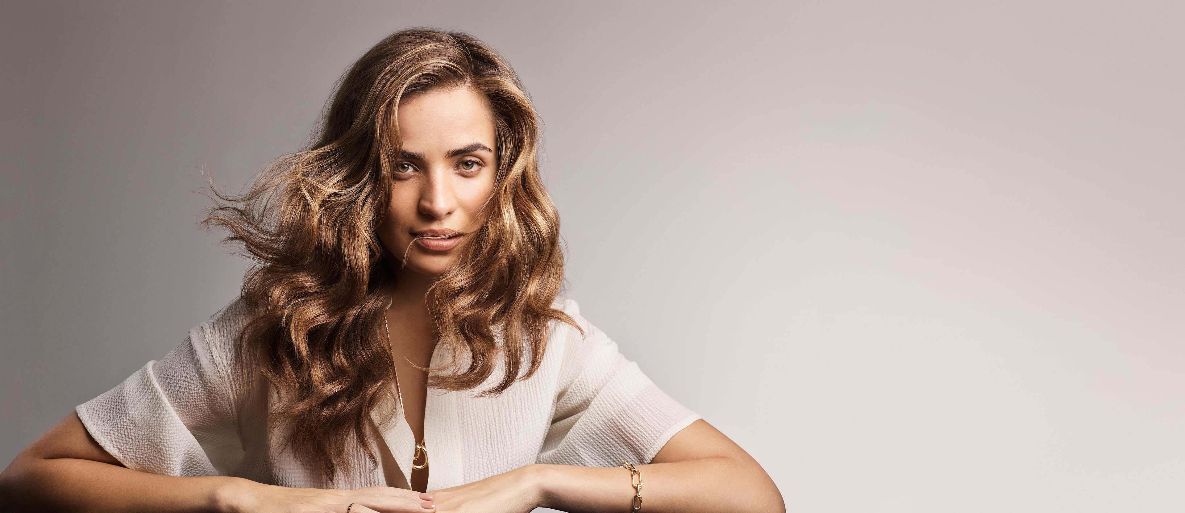 Woman with wavy hair wearing a light-colored top against a plain background